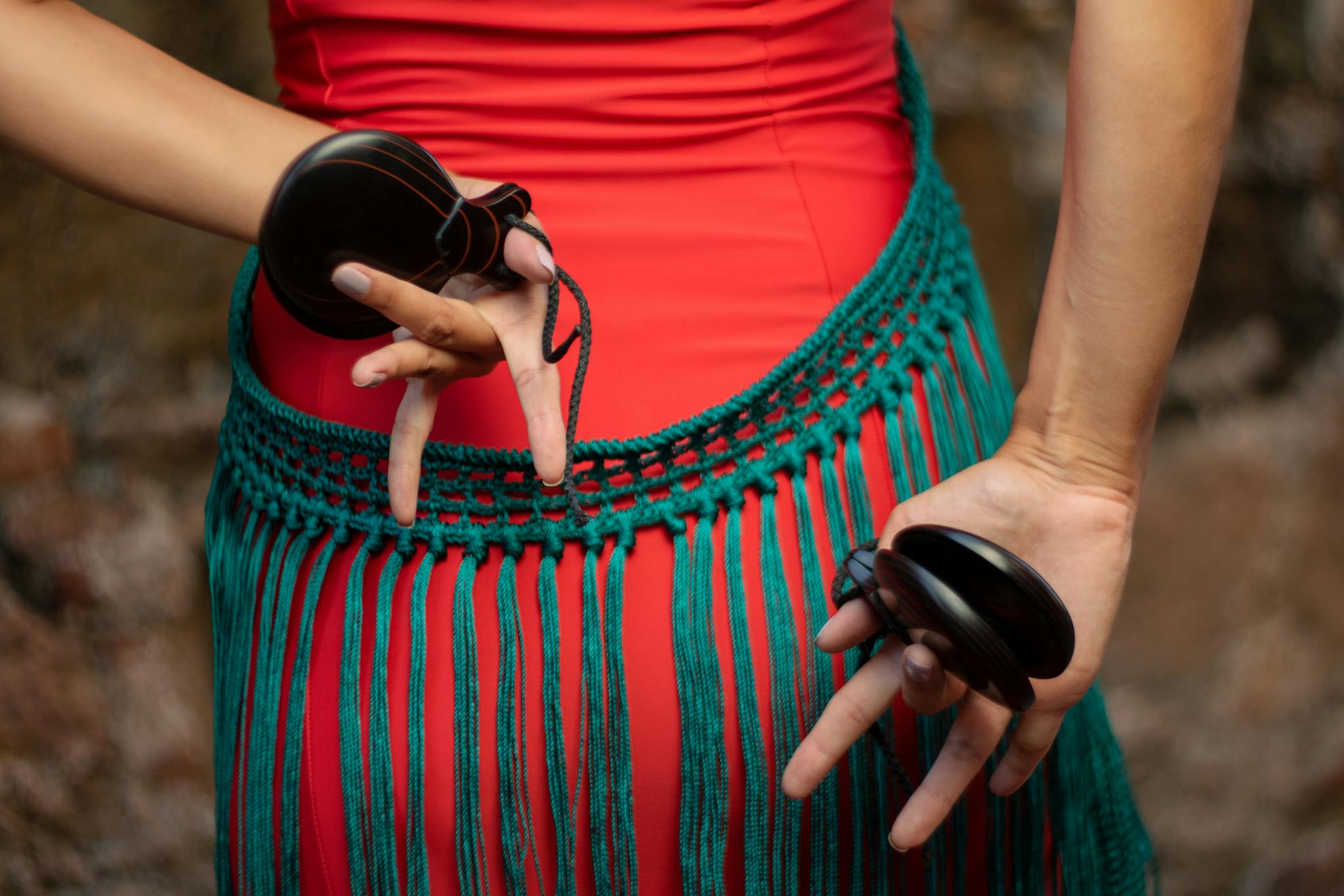 A close-up of a dancer's hands holding castanets with a colorful costume detail.