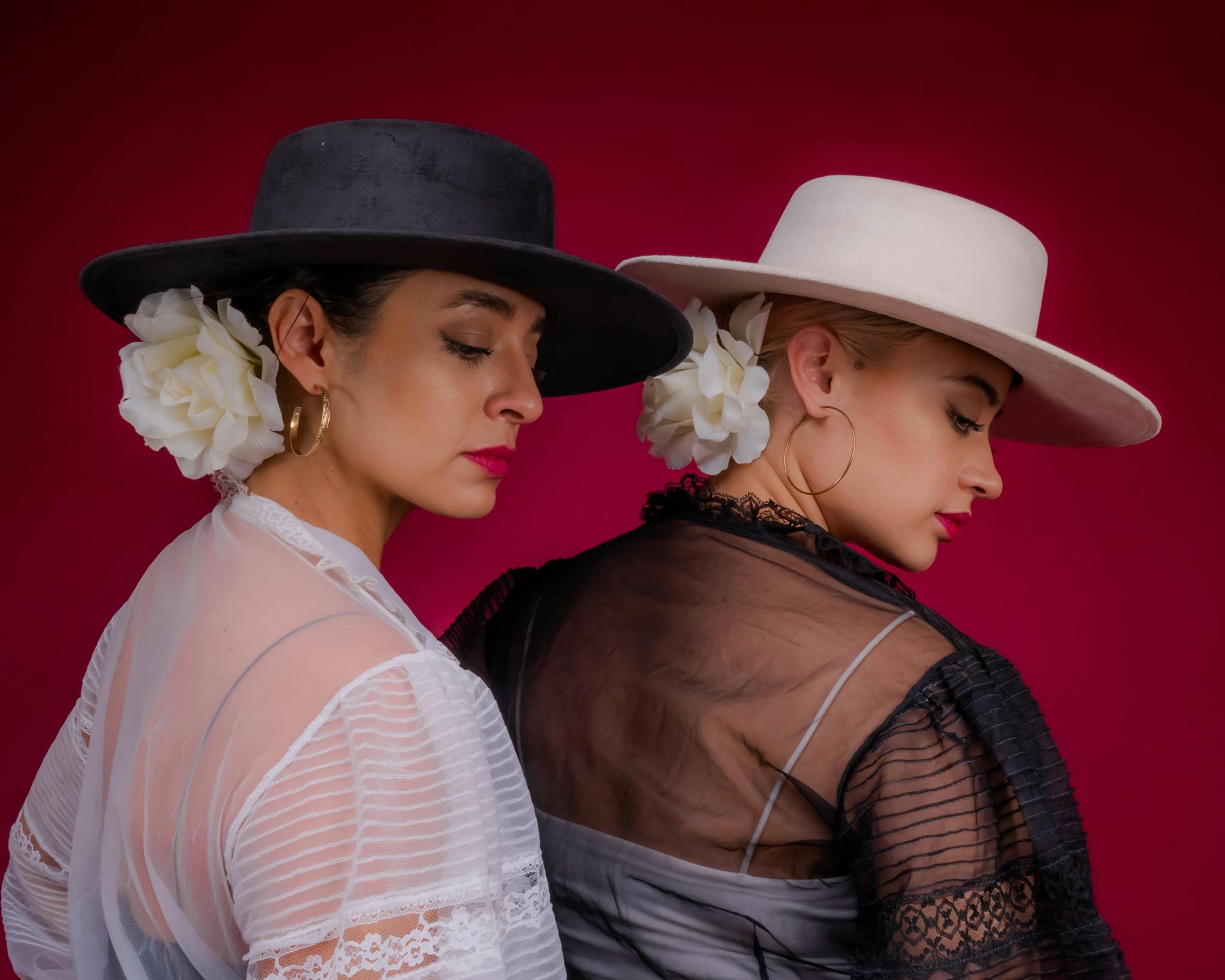 Stunning artistic portrait of two flamenco dancers in traditional Spanish attire against a deep red background.